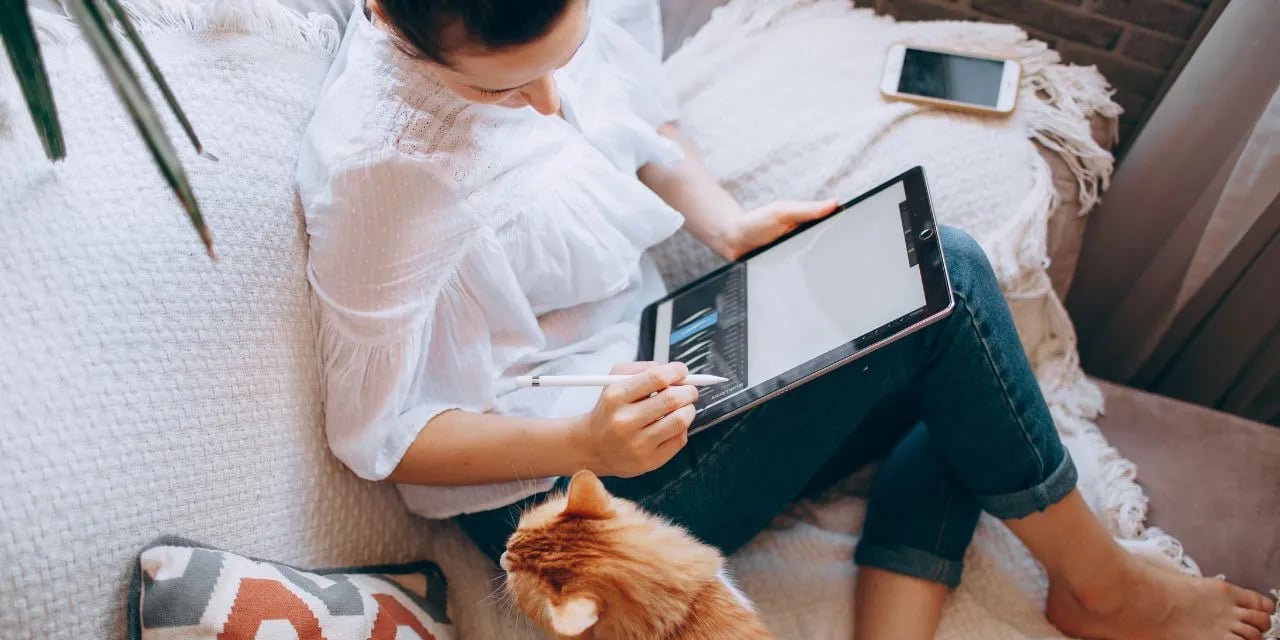 Une femme travaille sur Photoshop en télétravail avec son chat depuis son canapé