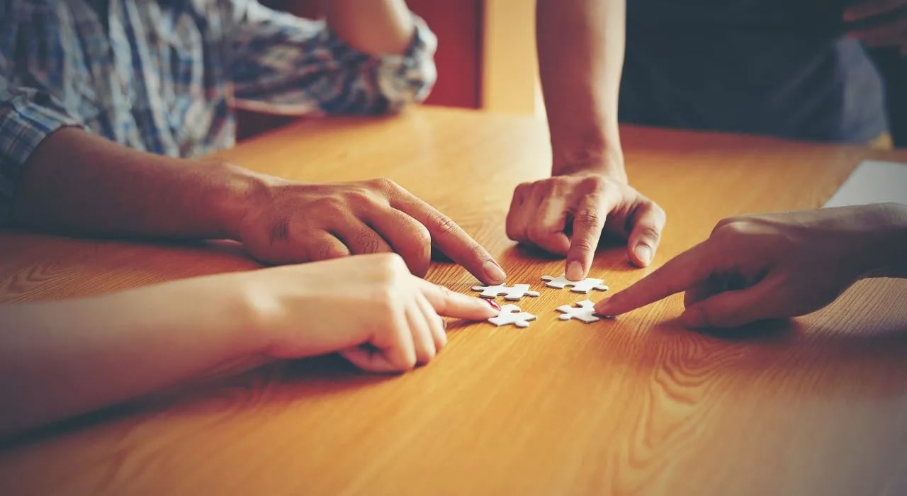 Mensen aan tafel die puzzelstukjes samenbrengen 