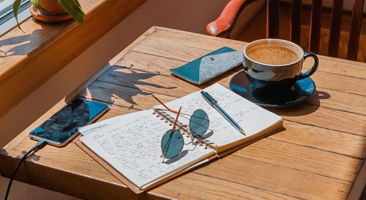 Un smartphone, un cahier, des lunettes et une tasse sont sur une table en terrasse