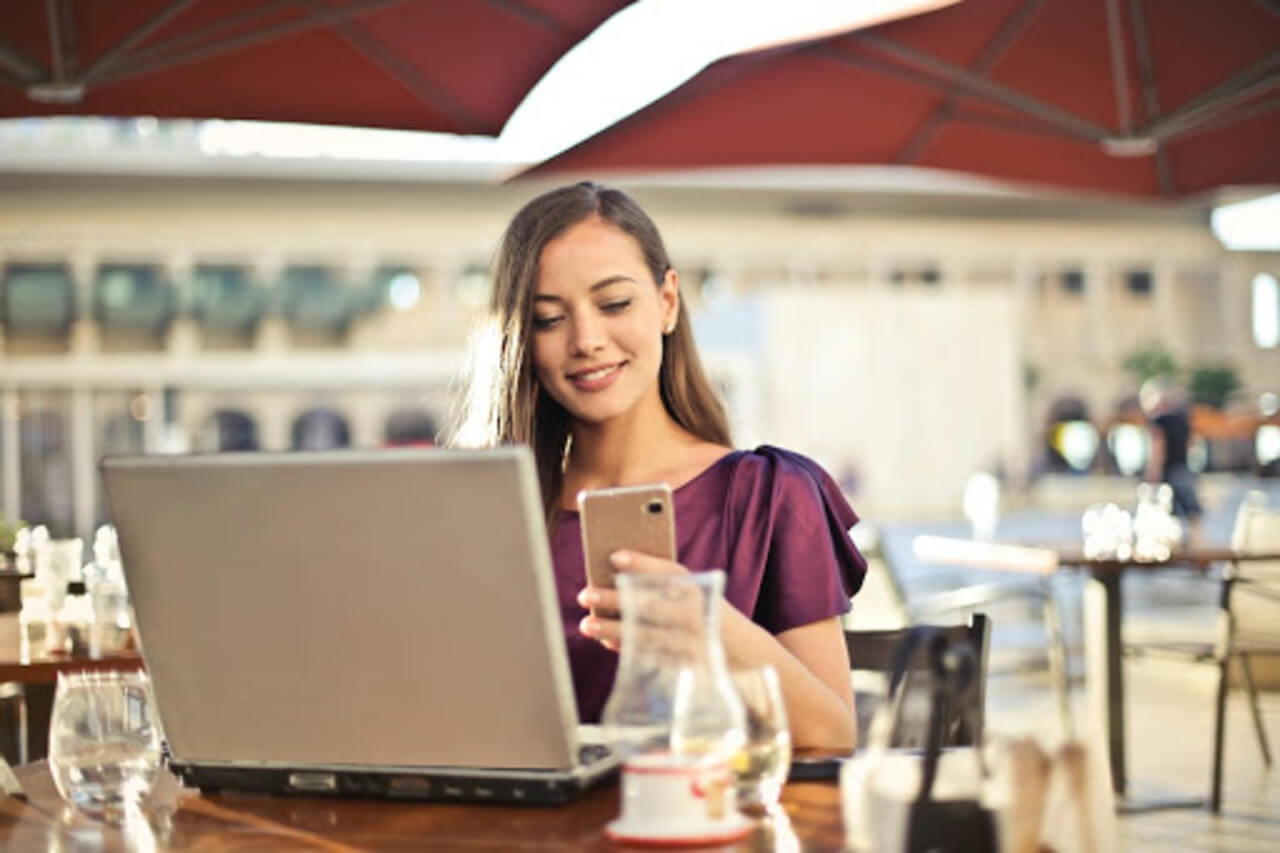 Woman using a laptop and mobile phone at an outdoor cafe