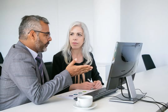 two-serious-managers-watching-presentation-pc-monitor-discussing-project-sitting-desk-with-paper-diagram-business-communication-concept-1-scaled